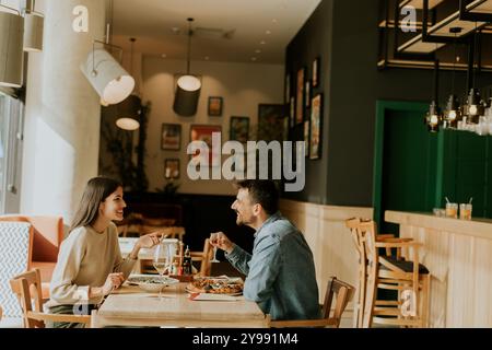 Un couple s'engage dans une conversation animée tout en savourant une délicieuse cuisine dans un restaurant lumineux, partageant des rires et des moments de connexion sur un lei Banque D'Images