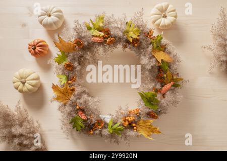 Couronne avec des fleurs oranges et des matériaux naturels secs sur fond beige en bois. Vue de dessus. BRICOLAGE. Atelier pour la décoration de jour de Thanksgiving faite à la main. Banque D'Images