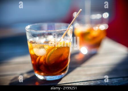 Un gros plan de deux verres remplis de cocktails rafraîchissants au vermouth sur une table de patio ensoleillée, soulignant les couleurs vives et l'ambiance accueillante. Banque D'Images