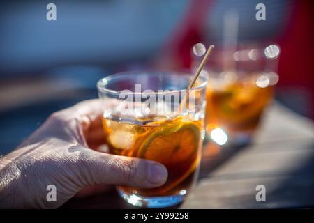 Une main d'homme tenant un verre de vermouth avec une tranche d'orange, capturant un cadre extérieur rafraîchissant et décontracté. Idéal pour les concepts de loisirs, rel Banque D'Images