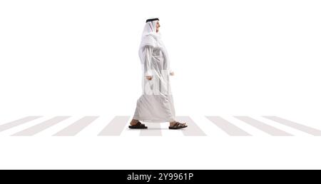 Plan de profil complet d'un homme arabe dans une thobe blanche et foulard marchant sur un passage piétonnier isolé sur fond blanc Banque D'Images