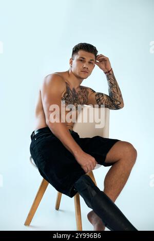 Un jeune homme avec des tatouages frappants met en valeur sa jambe prothétique tout en étant assis dans un studio moderne. Banque D'Images