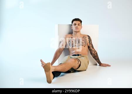 Un jeune homme tatoué présente sa jambe prothétique tout en se prélassant sur une toile de fond de studio. Banque D'Images