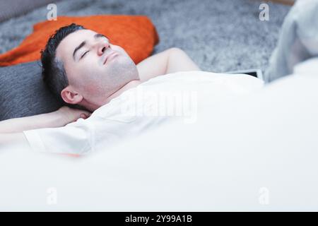 Jeune homme allongé sur le sol, les yeux fermés, profitant d'une sieste paisible dans un salon confortable Banque D'Images