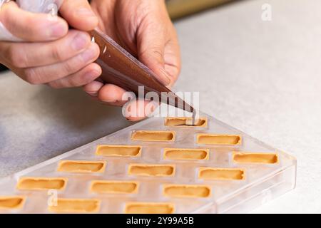 Chocolatier verse soigneusement du chocolat noir fondu dans un moule à bonbons, créant de délicieux et beaux chocolats. Mise au point sélective Banque D'Images