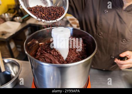 Chocolatier ajoutant des pointes de cacao dans une machine de melanger professionnelle pour la fabrication du chocolat. Mise au point sélective Banque D'Images