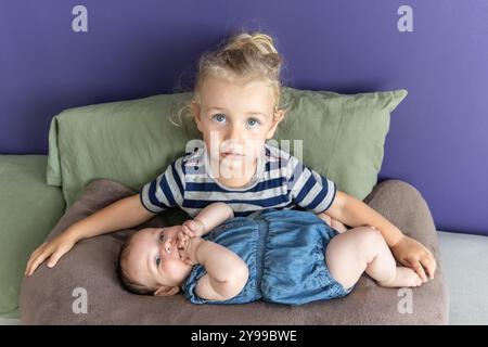 Big Brother tient sa petite sœur, qui suce sur ses doigts, tout en étant assis sur une chaise de pouf. Mise au point sélective Banque D'Images