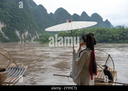 Fille de la dynastie Han avec de longs cheveux et un parapluie à côté d'un cormoran sur la rivière Li. Xingping, Chine Banque D'Images