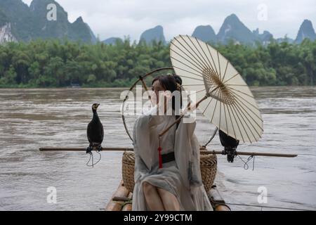 Hanfu fille fixant ses cheveux et tenant parasol tout en se tenant debout sur un radeau de bambou près de la rivière Li Banque D'Images