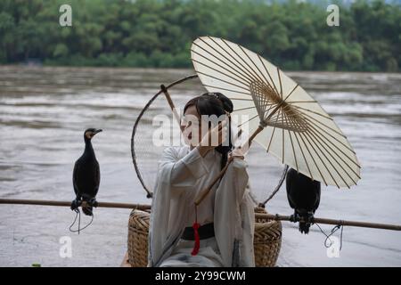 Hanfu fille fixant ses cheveux et tenant parasol tout en se tenant debout sur un radeau de bambou près de la rivière Li Banque D'Images