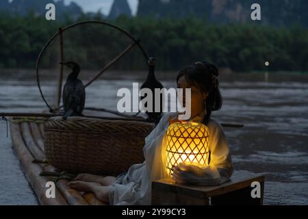 Hanfu fille tenant une lanterne illuminée sur un radeau de bambou avec des oiseaux Cormoran la nuit Banque D'Images