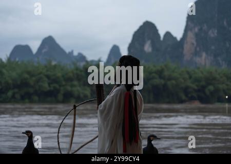 Fille Hanfu debout dans la rivière Li avec oiseau de pêche Cormoran perché sur un radeau de bambou Banque D'Images