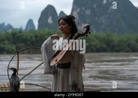 Hanfu Girl souriant au-dessus de Li River met un instrument traditionnel de pipa dans son dos Banque D'Images