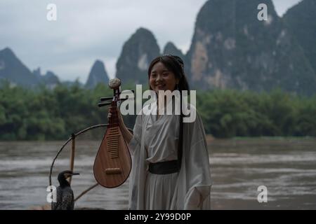 Hanfu Girl souriant au-dessus de Li River met un instrument traditionnel de pipa dans son dos Banque D'Images