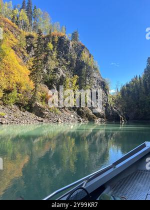 Vue sereine de la rivière Bulkley en Colombie-Britannique, Canada, entourée de feuillage d'automne et de falaises rocheuses, capturée depuis un bateau sous un ciel bleu clair Banque D'Images