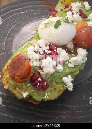 Toast à l'avocat garni d'un œuf poché, de fromage feta, de tomates rôties et de microgreens, servi sur du pain rustique pour un repas frais et délicieux Banque D'Images