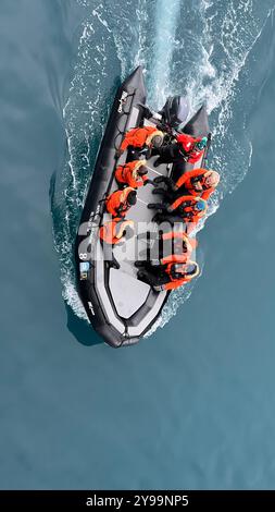 Une vue aérienne d'un petit bateau d'expédition transportant des passagers dans des vestes orange vif alors qu'ils explorent les eaux de l'Antarctique Banque D'Images