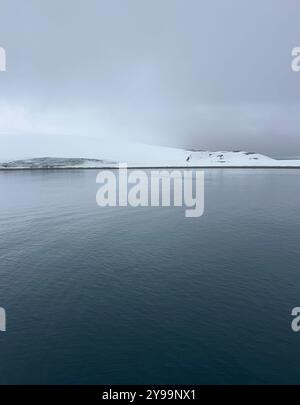 Une vue sereine sur l'océan Austral en Antarctique, avec des eaux lisses reflétant le ciel couvert et le paysage enneigé Banque D'Images