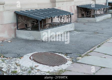 Grille décorative au-dessus d'une fenêtre de sous-sol sur un Streetside pavé. Banque D'Images