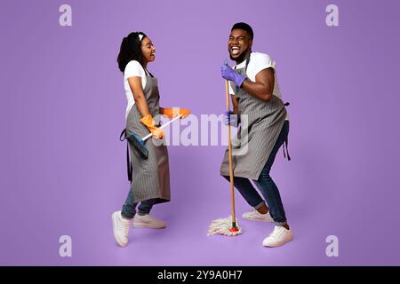 Concept de service d'entretien joyeux. Couple africain joyeux de nettoyeurs ayant du plaisir pendant les tâches Banque D'Images