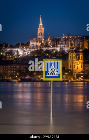 Panneau de signalisation sortant du Danube pendant les inondations à Budapest la nuit, avec l'église Matthias et le bastion des pêcheurs en arrière-plan Banque D'Images