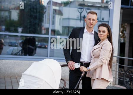 Couple élégant posant avec une poussette de bébé dans un cadre urbain. Banque D'Images