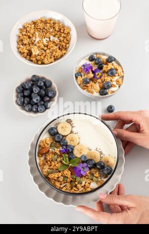 Les mains des femmes tiennent un bol de yaourt grec, de granola et de baies. Petit déjeuner. Banque D'Images