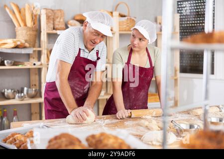 Les boulangers homme et femme déroulent la pâte avec un rouleau à pâtisserie Banque D'Images