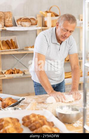 Homme senior travaille comme boulanger dans la boulangerie, moule les tartes à partir de pâte, crée des croissants à partir de pâte. Banque D'Images