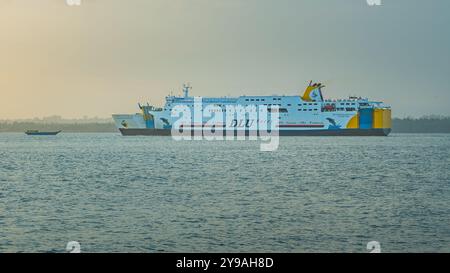 Balikpapan, Indonésie - 9 octobre 2024. Le ferry glisse sur des eaux calmes, illuminées par les teintes chaudes d'un soleil couchant. Des bateaux plus petits parsèment le Banque D'Images