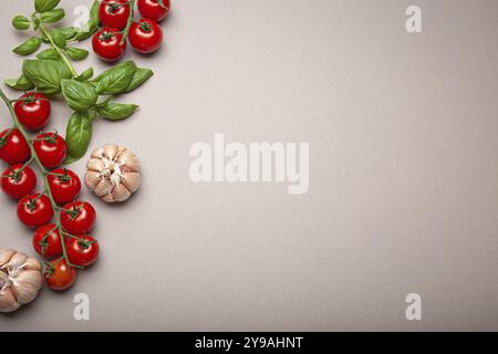 Composition avec branche de tomates cerises fraîches, basilic, gousses d'ail, quartiers de citron, sur fond minimaliste gris propre, prise de vue aérienne avec copie s. Banque D'Images