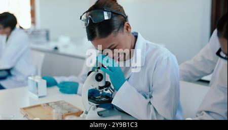 Science, étudiant et étude avec microscope en laboratoire pour l'analyse d'échantillons, leçon pratique et éducation. Lycéenne, examiner et apprendre Banque D'Images