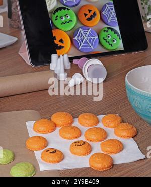 Macarons d'Halloween. Citrouilles et monstres dessinent avec marqueur alimentaire dans la cuisine. Cuisson de macarons à la maison en gros plan. Banque D'Images