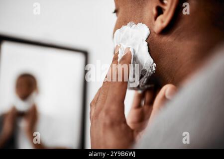 Homme, barbe et crème à raser avec miroir pour le toilettage, mousse ou après-rasage dans la salle de bain à la maison. Gros plan, personne masculine ou l'application de lotion, savon ou Banque D'Images