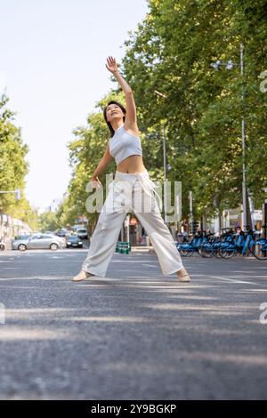 Jeune femme danse gracieusement dans une rue de la ville, exsudant joie et liberté sous le ciel ensoleillé. Ses mouvements mettent en valeur la créativité et la passion, incarnant un style de vie actif Banque D'Images