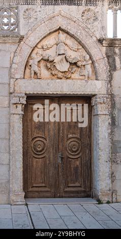 Rab, Croatie - 19 août 2023 : une porte historique en bois dans une arche en pierre, ornée de sculptures complexes et de motifs de pierre ornés Banque D'Images