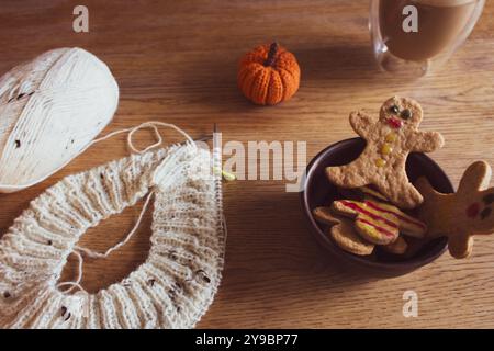 Biscuits homme en pain d'épice avec tasse à café et tweed blanc tricotant sur des aiguilles rondes. Biscuit décoré avec sourire et crochet avec citrouille tricotée Banque D'Images