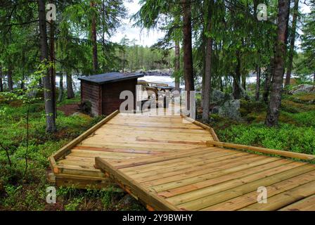 Sentier en bois sinueux menant à travers une forêt luxuriante à une cabane confortable nichée sur les rives d'un lac serein Banque D'Images