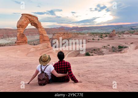 Couple en voyage de randonnée de vacances. Homme et femme assis au sommet de la montagne regardant une belle vue. Delicate Arch, Moab, Utah, Arches National par Banque D'Images