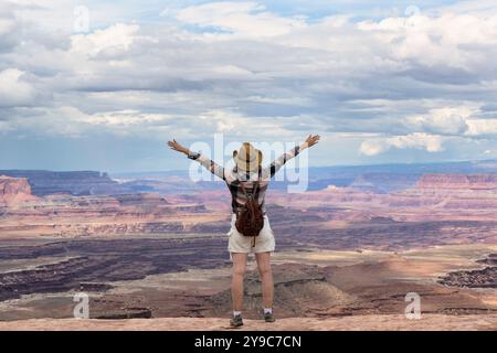 Femme aventureuse sur le bord d'une falaise regarde une belle vue de paysage dans le Canyon pendant un coucher de soleil vibrant. Utah, États-Unis. Banque D'Images