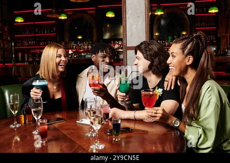 Un groupe animé profite de cocktails colorés et de rires lors d'une réunion d'entreprise la nuit. Banque D'Images