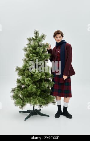 Une belle femme habillée dans la mode hivernale confortable se tient à côté d'un arbre de fête, exsudant le charme. Banque D'Images