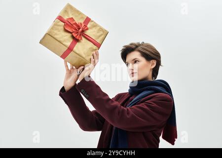 Une femme élégamment habillée en tenue d'hiver admire un cadeau avec un ruban vibrant à la main. Banque D'Images