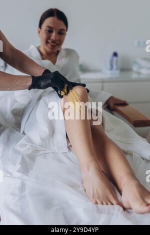 Esthéticienne épilant les jambes d'une jeune femme au sucre liquide en centre thermal. Photo de haute qualité Banque D'Images