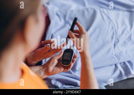 Une infirmière vérifie le taux de sucre dans le sang d'un homme âgé tout en étant assise à côté de lui et en piquant son doigt avec une aiguille. Photo de haute qualité Banque D'Images