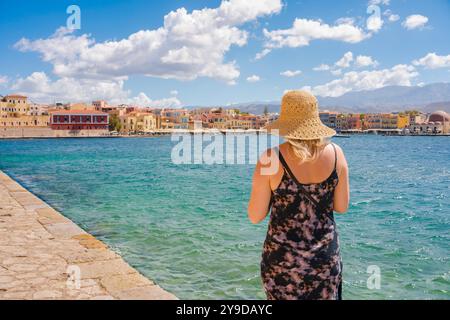 Vacances d'été, vue arrière d'une jeune femme blonde portant un chapeau d'été regardant à travers le port intérieur à Chania (Hania), nord-ouest de la Crète, Grèce Banque D'Images
