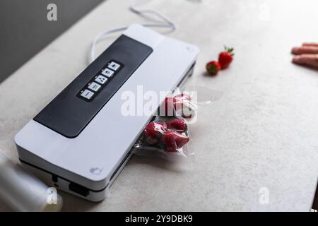 la main d'un homme utilise une machine à vide pour emballer les fraises sous vide dans des sacs en plastique. . Photo de haute qualité Banque D'Images