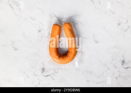 Vue de dessus d'une saucisse fumée hollandaise traditionnelle emballée sous vide dans du plastique sur un fond de marbre. Banque D'Images