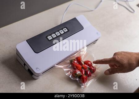 la main d'un homme utilise une machine à vide pour emballer les fraises sous vide dans des sacs en plastique. . Photo de haute qualité Banque D'Images