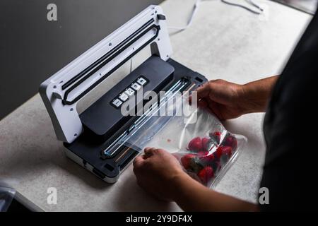 la main d'un homme utilise une machine à vide pour emballer les fraises sous vide dans des sacs en plastique. . Photo de haute qualité Banque D'Images